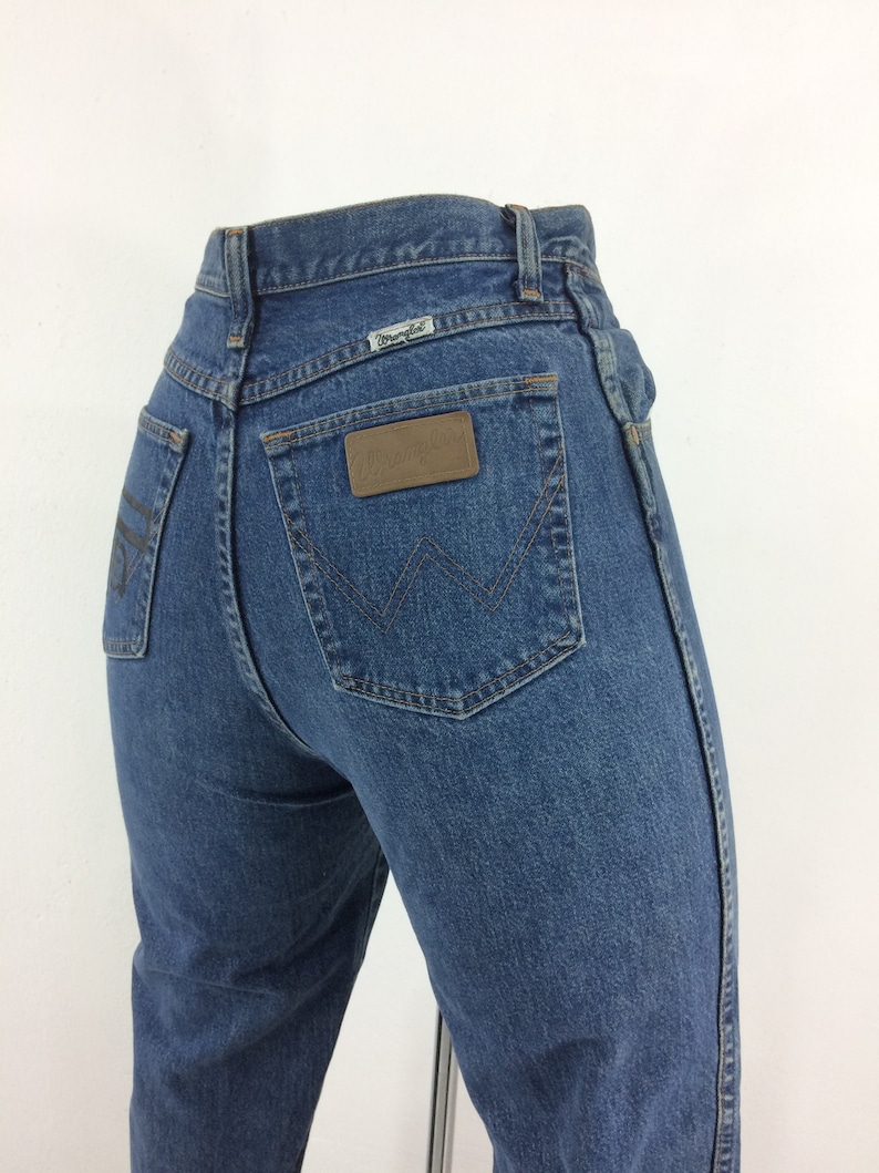 May include: A pair of blue denim jeans with a brown leather patch on the back pocket that says "Wrangler".