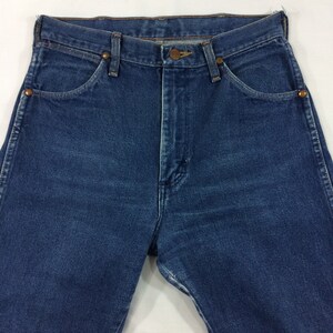 May include: Close-up of a pair of blue denim jeans. The jeans have a classic five-pocket design, a button and zipper closure, and copper-colored rivets. The denim has a medium wash and a slightly worn appearance.