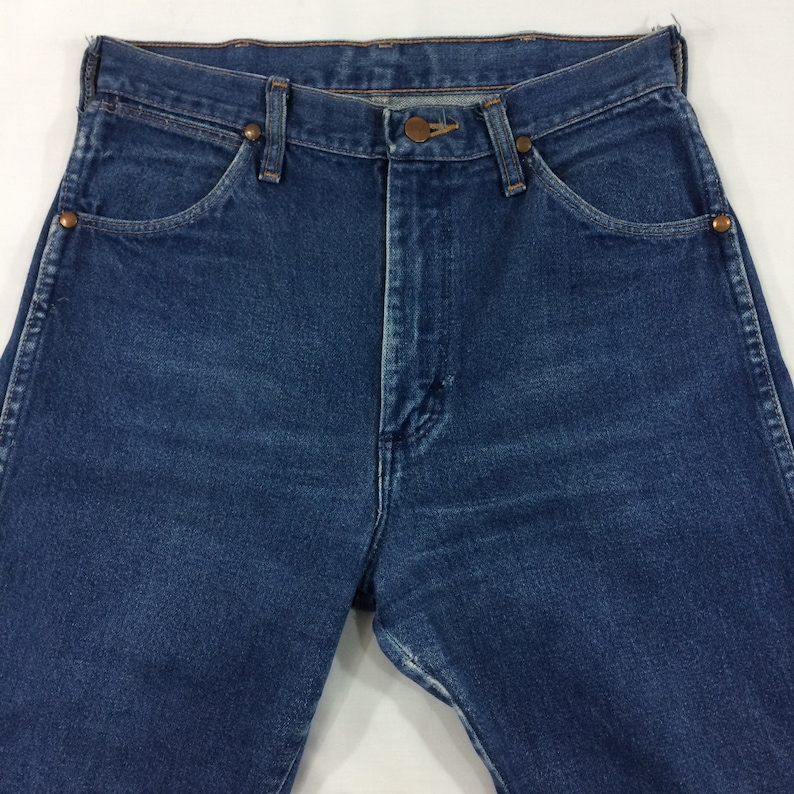 May include: Close-up of a pair of blue denim jeans. The jeans have a classic five-pocket design, a button and zipper closure, and copper-colored rivets. The denim has a medium wash and a slightly worn appearance.
