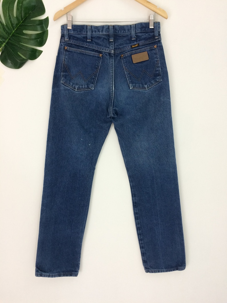 May include: A pair of blue denim jeans with a brown leather patch on the back pocket that says "Wrangler".
