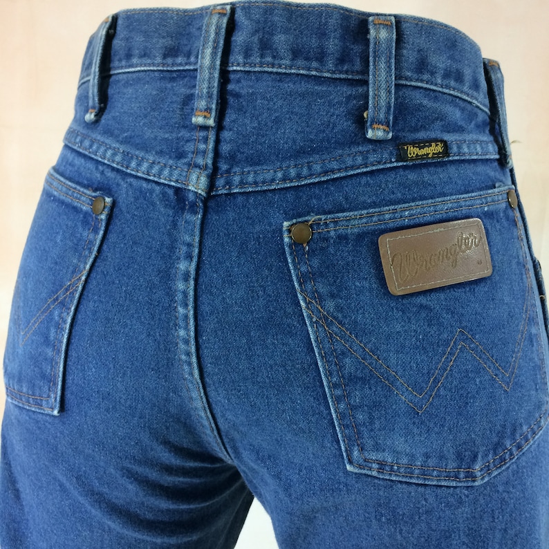 Vintage Wrangler Jeans 29 30 Waist High Waisted Jeans. Vintage high-waisted Wrangler jeans in a dark indigo wash denim. Front metal zipper, belt loops, 4 pockets, black "Wrangler" label & 100% cotton Made In USA.