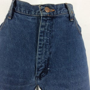 May include: Close-up of the front of a pair of blue denim jeans. The jeans have a button fly and a copper-colored button. The fabric is a medium-wash denim.