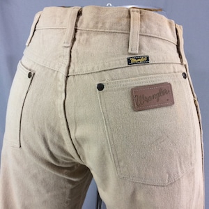 May include: A pair of light brown Wrangler jeans with a brown leather patch on the back pocket that says "Wrangler".