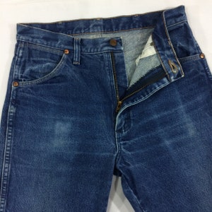 May include: A pair of blue denim jeans with a zipper fly and a copper button. The jeans have a classic five-pocket style and a faded look.