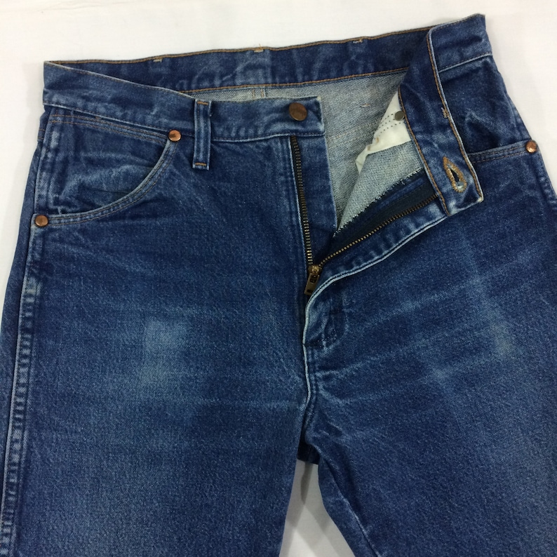 May include: A pair of blue denim jeans with a zipper fly and a copper button. The jeans have a classic five-pocket style and a faded look.