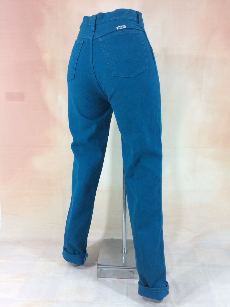 May include: Teal blue high-waisted jeans with a Wrangler label on the back pocket.