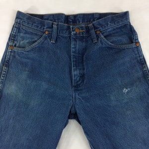 May include: A pair of blue denim jeans with a faded look and a small hole on the right leg.