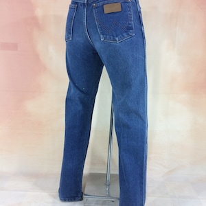 May include: A pair of blue denim jeans with a brown leather patch on the back pocket that says "Wrangler".