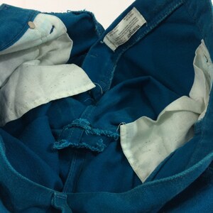 May include: Close-up of the inside of a pair of teal blue denim jeans with a white Wrangler label. The label has the text "Wrangler" and "Made in USA" printed on it.