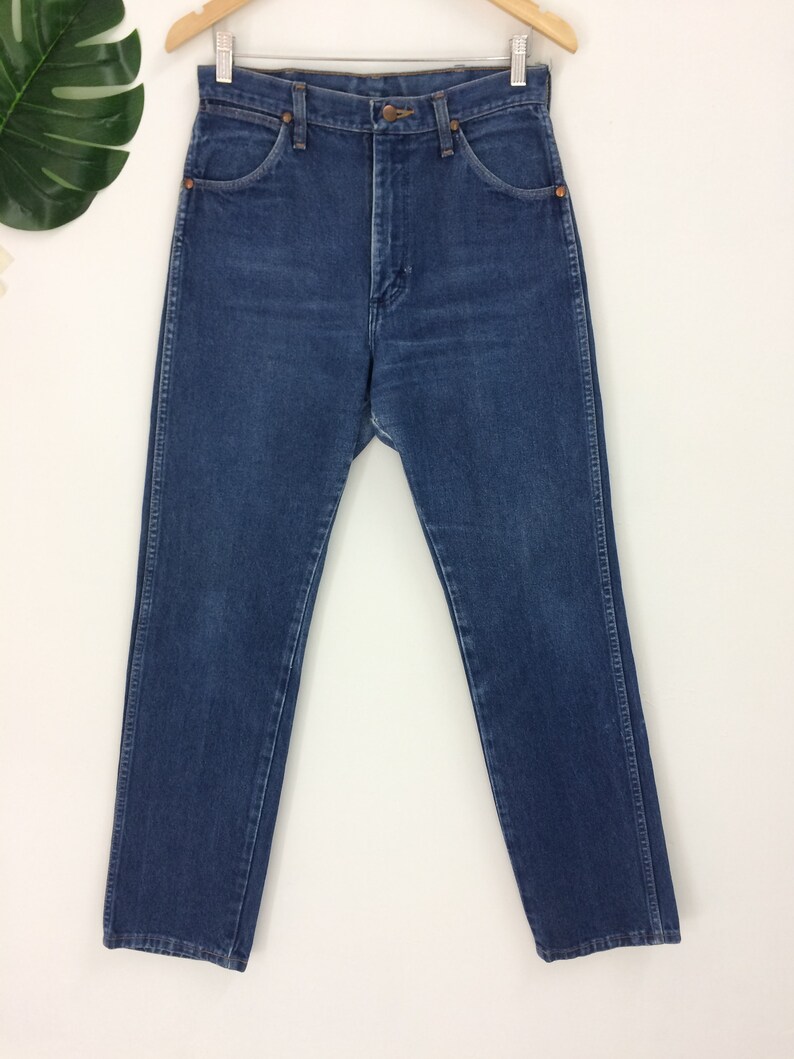 May include: A pair of blue denim jeans hanging on a wooden hanger. The jeans have a classic five-pocket design, a button and zipper closure, and a straight leg cut. The denim has a medium wash with subtle fading.