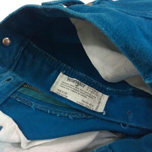 May include: A teal blue pair of Wrangler jeans with a white care label that reads "Machine wash with like colors, only non-chlorine bleach when needed, tumble dry, remove promptly. Made in USA 100% Cotton. M486-018 0 84084 324023"