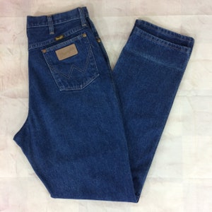 May include: Blue denim jeans with the Wrangler logo on the back pocket. The jeans have a classic five-pocket design, a button and zipper closure, and a straight leg fit. The jeans are a medium wash and appear to be in good condition.