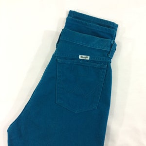 May include: A pair of teal blue denim jeans with a back pocket and a Wrangler label.