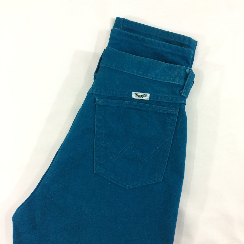 May include: A pair of teal blue denim jeans with a back pocket and a Wrangler label.