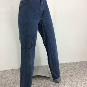 May include: A pair of blue denim jeans with a black graphic of fish on the left leg.