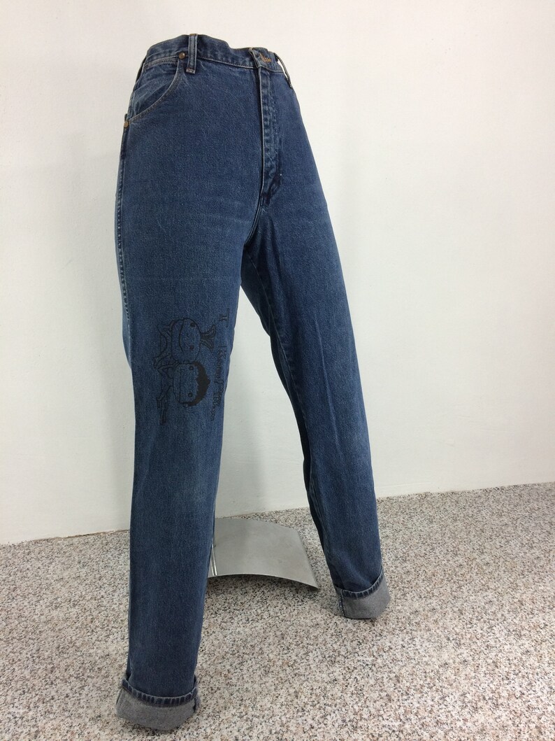 May include: A pair of blue denim jeans with a black graphic of fish on the left leg.