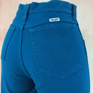 May include: A pair of teal blue denim jeans with a back pocket featuring a white "Wrangler" logo.