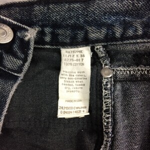 May include: Close-up of dark wash denim jeans. The tag reads "NA732MK 11/12 X 36 A275-017 100% COTTON". The jeans have a button closure and a stitched seam. The tag also includes washing instructions and "MADE IN USA".