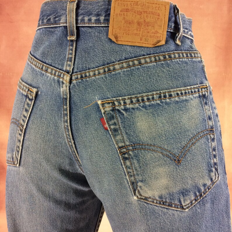 May include: A pair of blue denim jeans with a brown leather Levi's patch on the back pocket. The patch has the text "Levi Strauss & Co. San Francisco, Cal.  Original  Quality  Clothing  Every Garment Guaranteed  W 32 L 32".