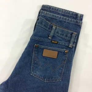 Peut inclure: Un jean en denim bleu avec un patch en cuir marron sur la poche arri&egrave;re qui dit "Wrangler".