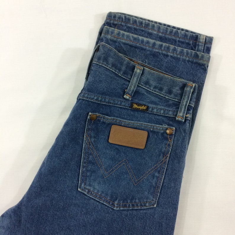 Peut inclure: Un jean en denim bleu avec un patch en cuir marron sur la poche arri&egrave;re qui dit "Wrangler".