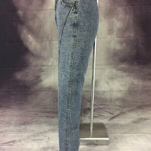 May include: Acid wash denim jeans with a unique diagonal seam detail on the front. The jeans have a classic five-pocket design and a straight leg fit. The hem is cuffed with a dark gray fabric.