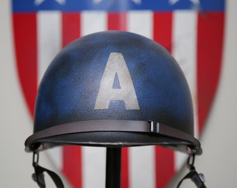 May include: A blue helmet with a white "A" on the front, featuring a brown chin strap. The helmet is displayed in front of a shield with red, white, and blue stripes.