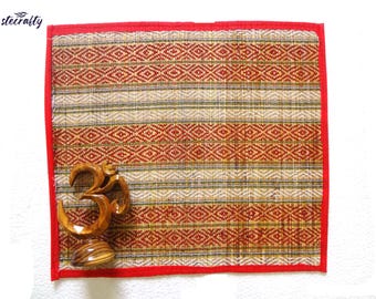 May include: A red and beige woven mat with a red border. A wooden Om symbol is placed on the mat.