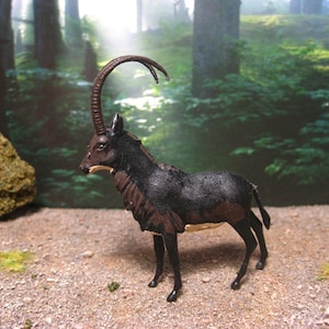 May include: Black and brown toy figure of a sable antelope with long, curved horns. The figure is standing on a gravel surface with a green forest background.