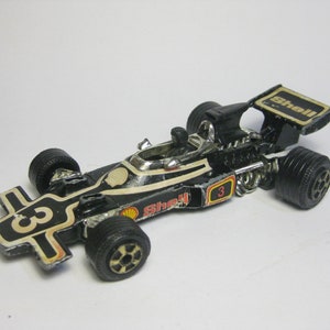 May include: Black and gold toy race car with a Shell logo and the number 3 on the side. The car has a black spoiler with the word "Shell" on it.