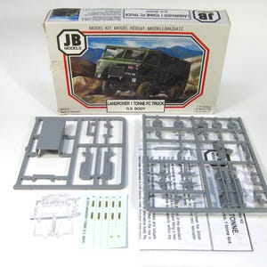 May include: A model kit of a Land Rover 1 Tonne FC Truck. The box features an image of the truck in a green color. The kit includes gray plastic parts, a clear plastic piece, and a sheet of decals. The box reads "JB Models".