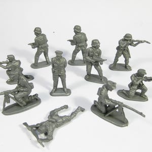 Puede incluir: Un conjunto de soldados de juguete de plástico gris en varias poses, incluyendo de pie, arrodillados y tumbados. Cada soldado sostiene un rifle o una ametralladora. Las figuras están sobre bases grises individuales, sobre un fondo blanco.