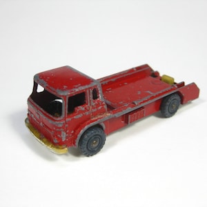 May include: A red toy truck with a flatbed and a yellow detail on the back. The truck has four wheels and is made of metal.