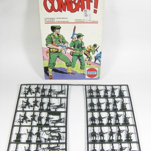 Puede incluir: Un juego de juguetes vintage titulado "COMBAT!" con una caja que muestra ilustraciones de soldados con uniformes verdes. Debajo, dos bastidores de plástico negro llenos de pequeños soldados de juguete de color verde oscuro en varias poses. La caja tiene texto en varios idiomas.