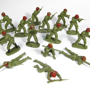 Peut inclure: Ensemble de soldats jouets en plastique vert, dans diverses poses d'action, debout, courant et couchés. Chaque soldat porte un casque rouge et porte un fusil. Les figurines sont sur des socles verts.