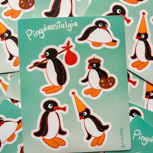 Puede incluir: Una hoja de pegatinas color verde azulado con varias ilustraciones de un pingüino blanco y negro con pico y patas naranjas. El texto Pinguinostalgia está impreso en blanco. Un pingüino lleva un hatillo rojo, otro lleva un gorro de fiesta.