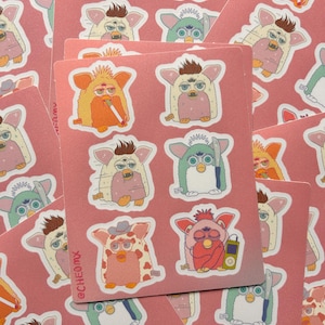 Puede incluir: Una hoja de pegatinas con seis ilustraciones distintas de juguetes Furby sobre un fondo rosa. Los personajes incluyen un Furby fumando, uno con un cuchillo, uno con sombrero de vaquero y uno escuchando un reproductor. El texto CHEOMX está impreso.