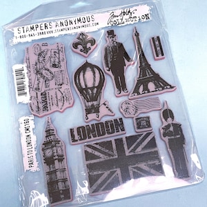 May include: A clear plastic package containing rubber stamps with a travel theme. The stamps feature images of the Eiffel Tower, Big Ben, a hot air balloon, and the text "LONDON" and "PARIS TO LONDON CMS160".