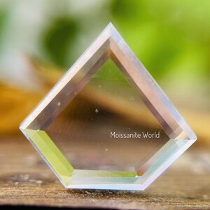 K&ouml;nnte beinhalten: Ein klarer, facettierter, sechseckiger Moissanit-Edelstein mit einem leichten Regenbogeneffekt. Der Edelstein liegt auf einer Holzoberfl&auml;che. Der Text "Moissanite World" ist auf dem Edelstein sichtbar.