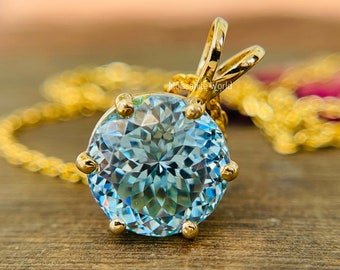 May include: A gold pendant necklace with a large, round, light blue gemstone. The gemstone is faceted and has a high shine.