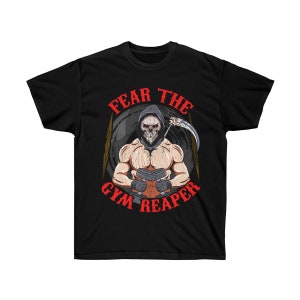 Puede incluir: Camiseta negra con un gráfico de un esqueleto musculoso que lleva una túnica con capucha y sostiene pesas. El texto "Fear the Gym Reaper" está escrito en rojo alrededor del esqueleto.