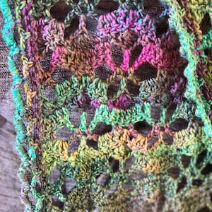 May include: A close-up of a crocheted scarf with a multi-colored pattern of green, blue, pink, and brown. The scarf has a delicate, lacy design.