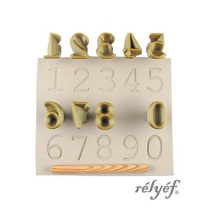 May include: A set of number-shaped molds and corresponding embossed numbers on a rectangular base. The molds are in a light brown color, with a wooden rolling pin. The brand name "rélyéf" is printed in the bottom right corner.