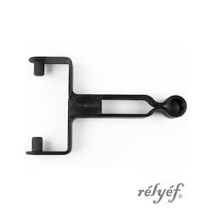 Op de afbeelding: Een zwart, uniek gevormd gereedschap met twee loodrecht op elkaar staande armen en een handvat met een afgerond uiteinde. Het woord "rélyéf" is in een scriptlettertype in de rechter benedenhoek gedrukt.