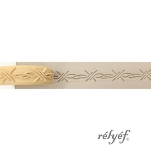 May include: A light beige rolling pin with a repeating barbed wire pattern. The pattern is pressed into a light grey surface. The word "rélyéf" is printed in a dark grey script font.