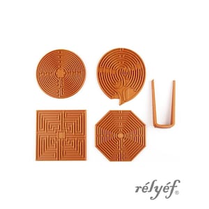 May include: A collection of orange-brown maze-shaped objects, including two circles, a square, an octagon, and a U-shaped piece. The objects have intricate, concentric designs. The brand name "rélyéf" is printed in a cursive font.