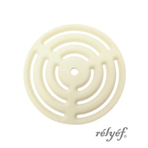 Op de afbeelding: Off-white keramische onderzetter met een cirkelvormig ontwerp met concentrische ringen en uitgesneden secties. De onderzetter heeft een klein centraal gat en het woord "rélyéf" staat rechtsonder gedrukt.