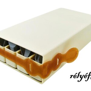 May include: A white rectangular box with a brown strap and a label that says "r&eacute;ly&eacute;f". The box has four compartments that are visible and appear to be filled with small items.