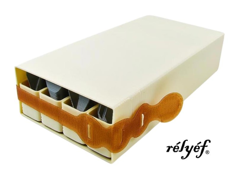 May include: A white rectangular box with a brown strap and a label that says "r&eacute;ly&eacute;f". The box has four compartments that are visible and appear to be filled with small items.