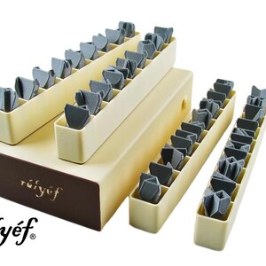 May include: A set of 36 gray plastic embossing stamps organized in three tiers of beige plastic trays. The trays are labeled "r&eacute;ly&eacute;f" in brown lettering.